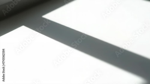 Shadow casting on a white wall creating abstract patterns. Sunlight streams through a window, highlighting clean and geometric lines on a minimalist surface.