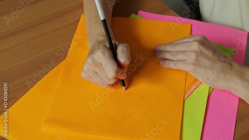 Top view of female hands drawing with pencil on colorful paper sheets