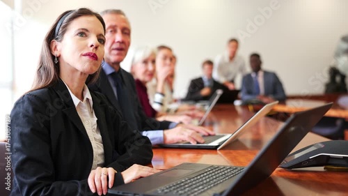 Mid aged white dark-haired male manager attending business meeting in conference room and interestedly watching colleague's presentation together with coworkers sitting