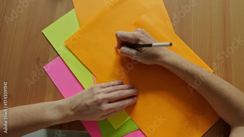 Top view of female hands drawing with pencil on colorful paper sheets