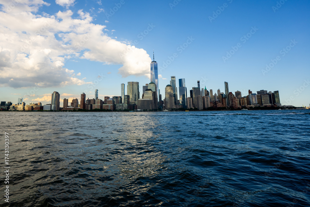 Fototapeta premium New York city. NYC cityscape. Lower Manhattan and One World Trade Center in New York Cit. Skyscrapers of Manhattan located near rippling water of New York bay against blue sky. New York skyscrapers.