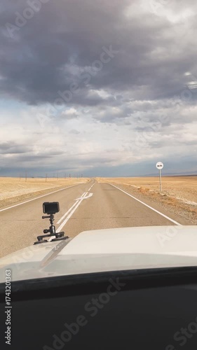 drive through the Kurai region of Altai during autumn. The open road stretches ahead, flanked by golden fields and mountains in the distance. Clouds loom overhead, adding drama to serene landscape.