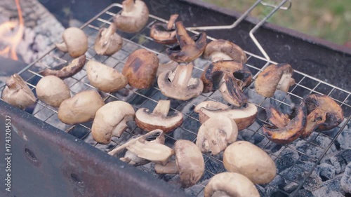 A grill grate with champignons is grilled over coals on a grill grate close-up. Enjoying a picnic outdoors with grilled mushrooms and delicious recipes for cooking champignons.