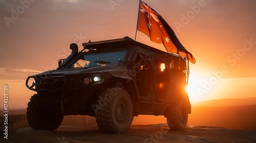 Patriotic Australian military vehicle silhouetted against dramatic orange sunset with red ensign flag flying, rugged all-terrain transport in outback landscape, defense forces patrol