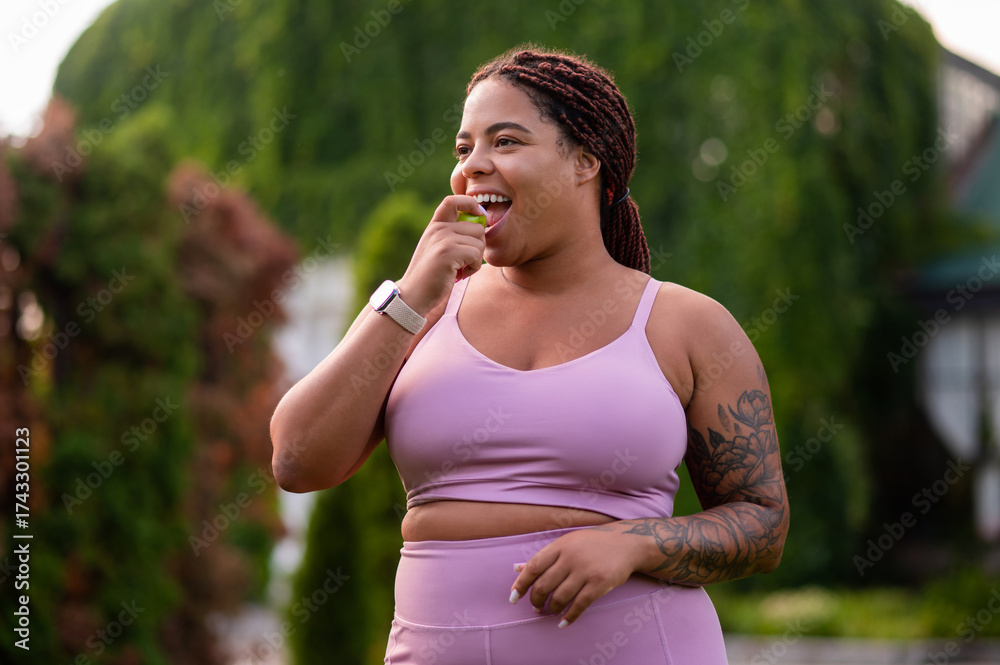 Fototapeta premium Young woman in pink sportswear outdoors with apple in hands