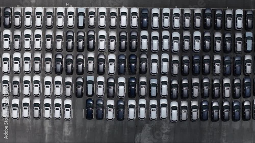 Aerial view of new cars in a large parking lot, arranged in geometric rows.