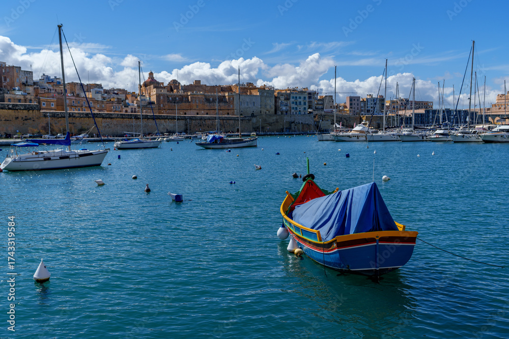 Fototapeta premium Traditional Luzzu Boat and Sailboats in Sunny Maltese Marina