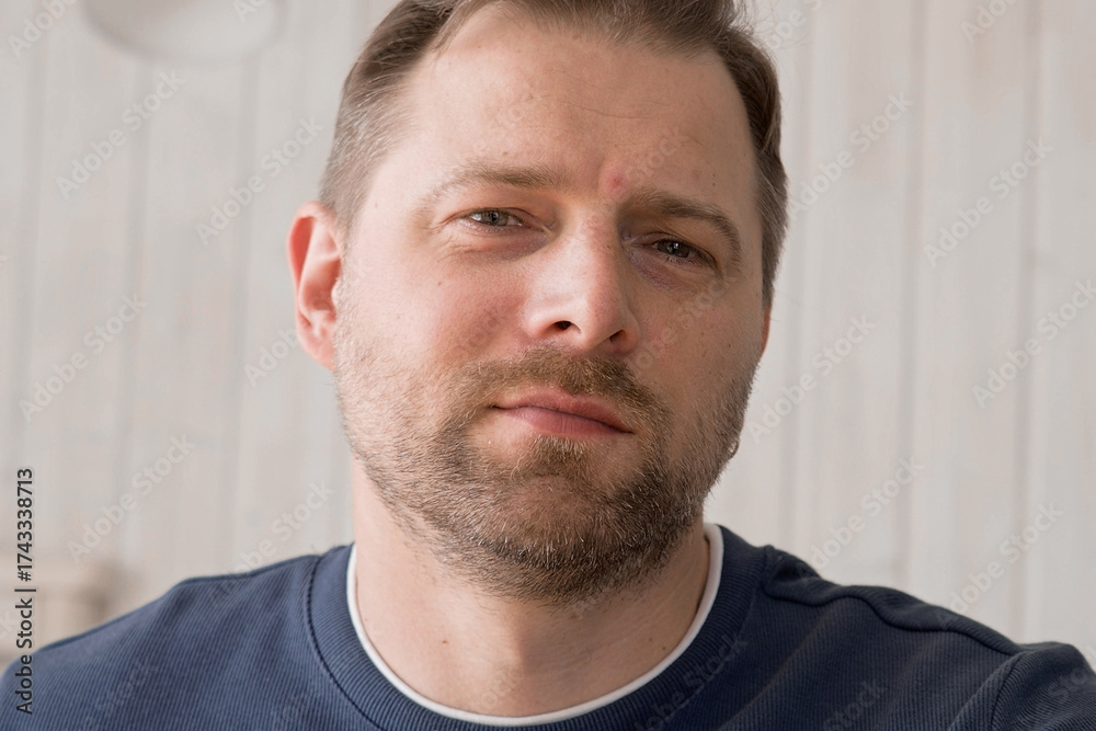Fototapeta premium Handsome young man in blue jersey indoors. Male with stylish haircut, beard feel happy, calm and serious. Home interior background. Man looking to camera and into distance. Diversity People. Portrait