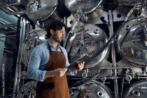 A man wearing an apron is holding a tablet inside a brewery facility