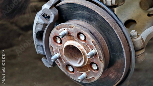 Closeup of a rusty car brake rotor showing wear and tear in a garage, highlighting the need for maintenance and repair, conveying a sense of neglect and mechanical issues.