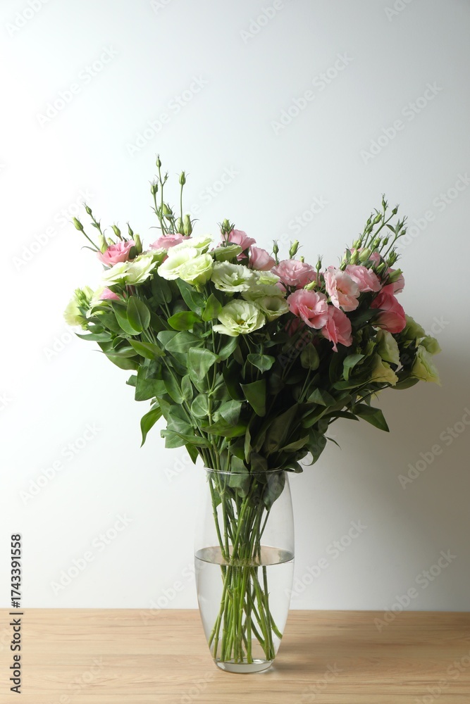 Fototapeta premium Eustoma flowers in a glass vase on table near white wall