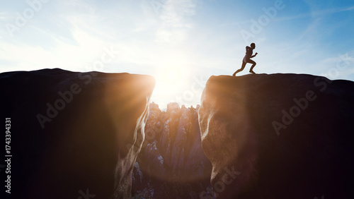 Tableau sur toile Silhouette of determined athlete running and jumping over a gap between two cliffs at sunset, symbolizing overcoming challenges and achieving goals