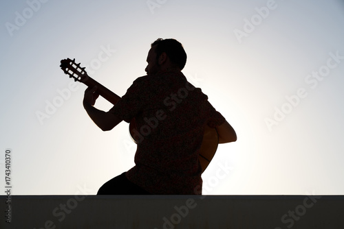 Foto Musician playing a flamenco guitar, silhouetted against a bright, clear sky