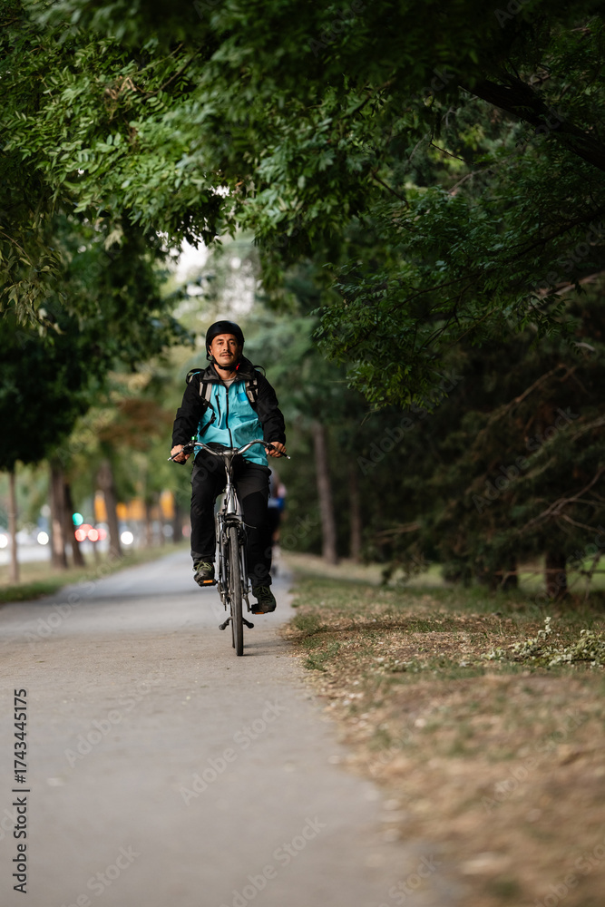 Obraz premium Courier riding bicycle in city park delivering food order