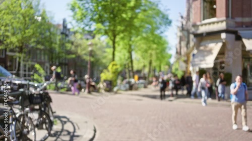 Wallpaper Mural Blurry scene of people walking along a sunny amsterdam street with bicycles and vibrant greenery enhancing the lively european city vibe. Torontodigital.ca