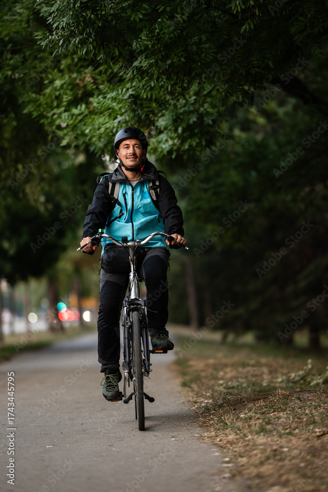 Fototapeta premium Smiling delivery man riding bicycle in city park