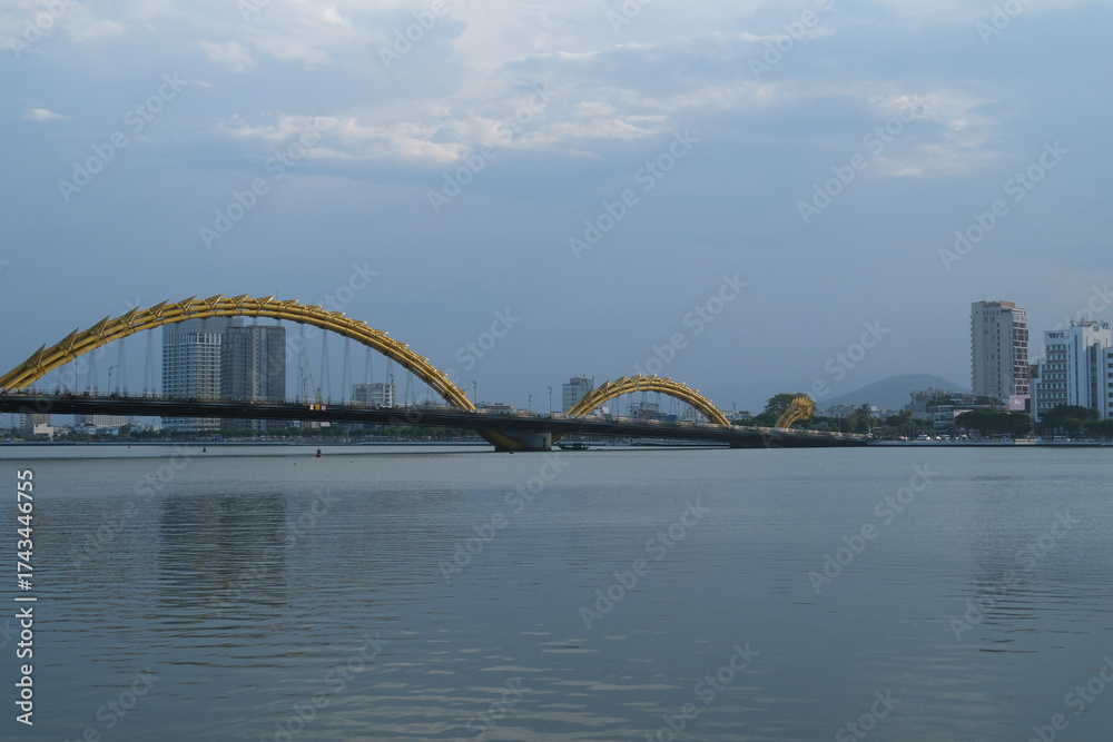 Fototapeta premium Scenic view of the iconic Dragon Bridge in Da Nang Vietnam spanning the Han River with steel dragon design illuminated by LED lights under sky reflection symbolizing urban growth and cultural identity