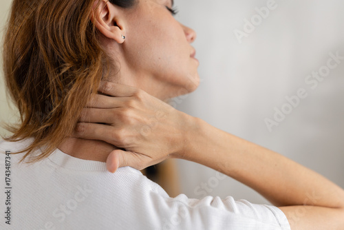 Close up rear view of woman touching her neck in pain, showing muscle tension or stiffness. Concept of neck pain, poor posture, stress, or office syndrome in daily life.