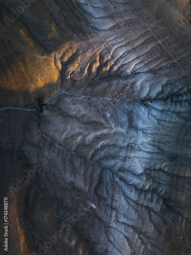 Aerial view of the stark, lunar-like landscape, where shadows deepen the rugged terrain's texture, contrasting the golden light, Goreme, Nevsehir, Turkiye.