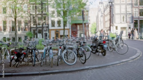 Blurred bicycles line the streets along amsterdam canals with defocused backgrounds displaying historic buildings and a bright, lively atmosphere in the netherlands.