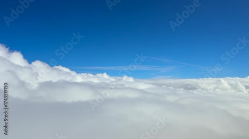 A pilot’s perspective from a jet cockpit in a smooth flight above and into an endless sea of white fluffy stratus clouds under a deep blue color sky. Ultra-realistic 4K shot.