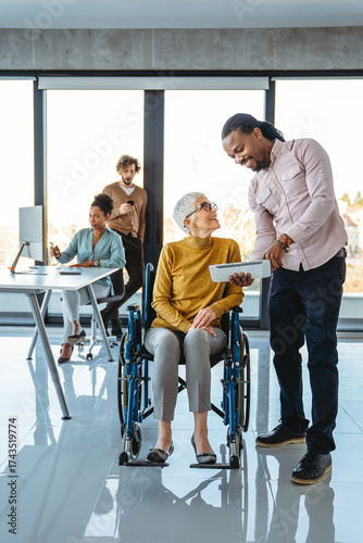 Business woman in wheelchair working with colleague in modern inclusive office. Diversity, support