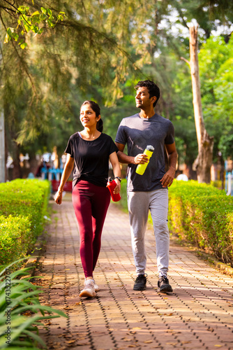 Indian couple walking together outdoors in morning sunlight, talking and enjoying nature in park
