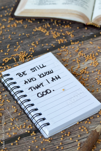 Be still and know that I am God, inspirational quote in notebook with mustard seeds on wooden background. Christian patience and faith in Jesus Christ, biblical concept.