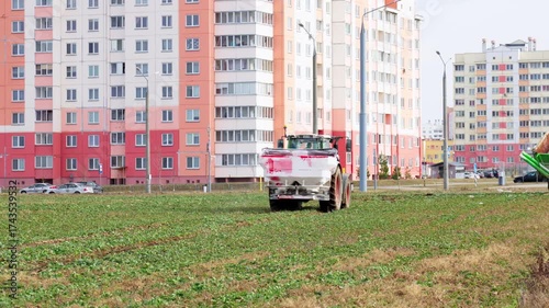 A wheel tractor spreads dry chemical fertilizer on a field in early spring. Agricultural work and soil preparation for the sowing season.