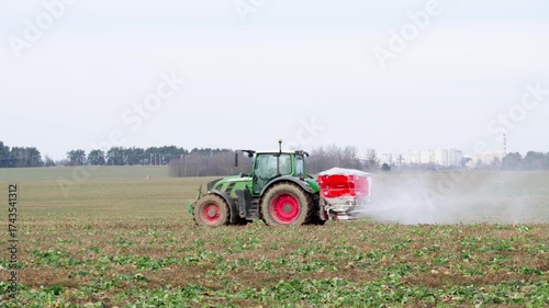 A wheel tractor spreads dry chemical fertilizer on a field in early spring. Agricultural work and soil preparation for the sowing season.