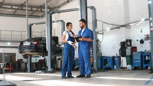 Digital tablet is in hands. Auto repair shop employees are working together. Man and woman