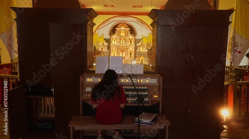 A wider shot of girl playing grand pipe organ in the Minor Basilica, Majayjay, Laguna, Philippines, ornate golden altar glowing behind with rich church details and warm light.