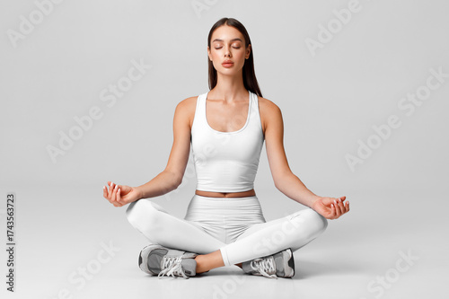 Fitness woman practicing yoga in lotus pose. Sporty female sitting in meditation on the gray background