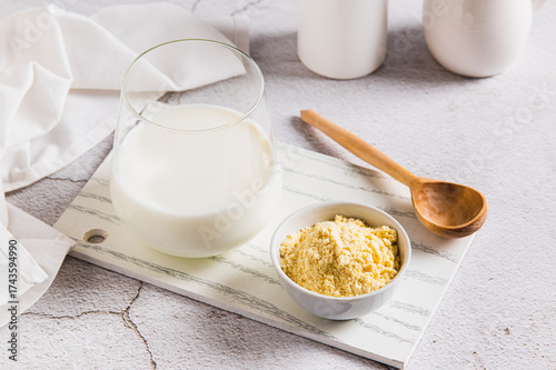 Bovine colostrum powder in a bowl and diluted drink in a glass on a table
