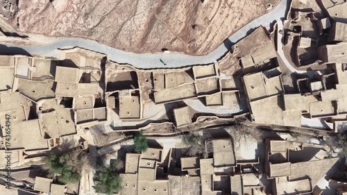 Aerial view of the ancient Tuyugou Xia Village reveals traditional mud-brick houses nestled between a winding road and arid landscape, Tuyugou Xia Village, China.