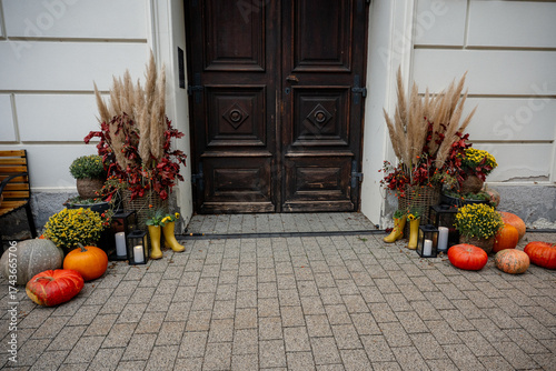 Front door decorated for autumn with pumpkins, gourds, colorful flowers, pampas grass, lanterns, yellow rain boots and rustic fall arrangements creating a cozy welcome