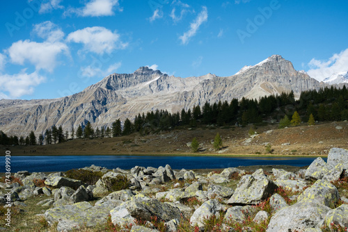 Panoramic view of Lake Dres in Gran Paradiso National Park, Piedmont, Italy. A sunny fall day with golden tones, snow-dusted peaks, and calm alpine reflections in a pristine mountain landscape