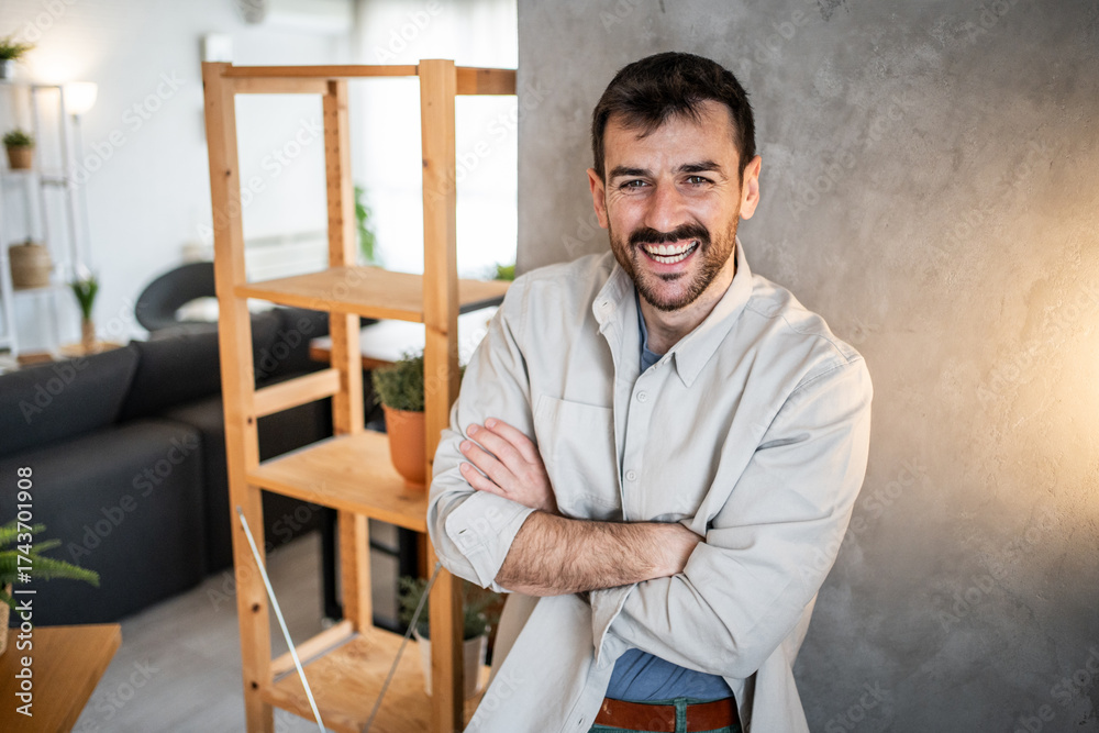 Fototapeta premium Smiling man standing cheerfully with crossed arms at home