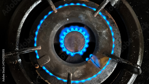 Wallpaper Mural Close-up of a lit gas stove burner with a vibrant blue flame emanating from the circular metal structure. Torontodigital.ca