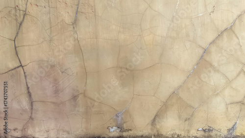 Cracked and weathered wall surface with a beige tone, showing signs of age an...