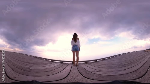 Woman standing on a wooden pier looking out at the sea with dramatic clouds in the sky during sunset - A peaceful moment of reflection
