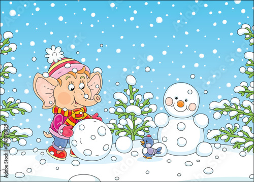 Cute little elephant playing with a merry small bird and making a big snowball for a toy snowman on a winter playground in a snowy park, vector cartoon illustration