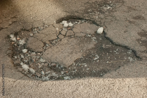 Asphalt road with a pothole, scattered clumps of poplar fluff on the surface, showing wear and outdoor detail.
