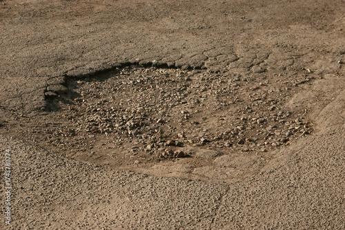A pothole in cracked asphalt on an old, damaged road, showing wear and decay.
