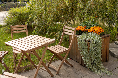 Wooden garden table with chairs and planter box with orange flowers on patio in daylight.
