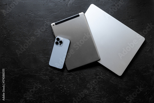 Silver laptop with tablet and mobile phone - high tech gadgets on black stone background, top view