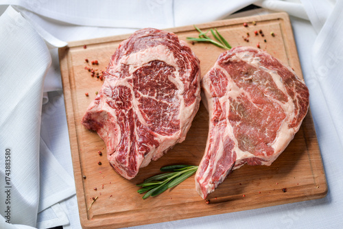 two huge raw steaks of meat on a wooden board