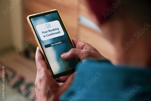 A South Asian man holding phone with Your booking is confirmed notification display. Selective focus on the text.