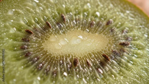 A macro close-up of a fresh kiwi fruit slice showing its vibrant green flesh, dark seeds, and glistening water droplets.