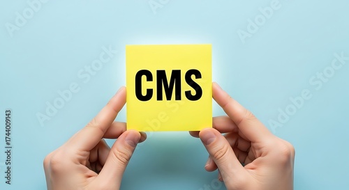 Hands holding a yellow sticky note with the text cms on blue background